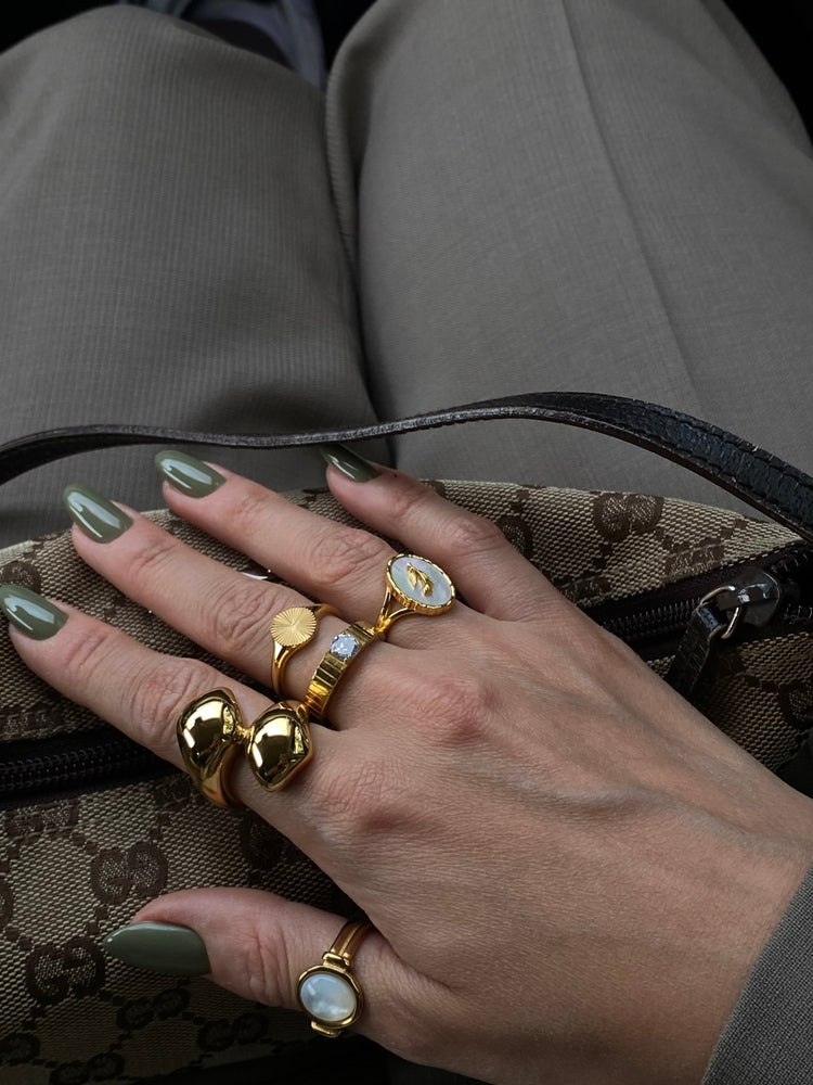 Neva Langais gold ring displayed among other stylish gold rings on a hand with green nails in a handbag.