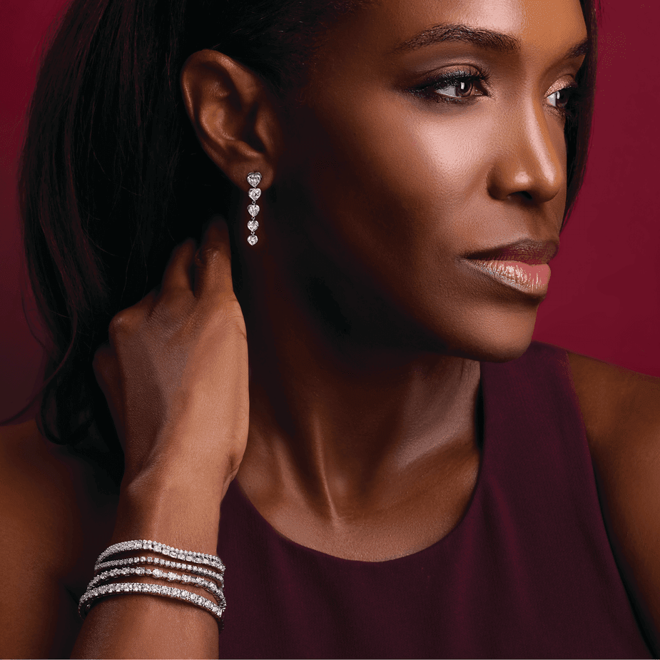 Elegant woman showcasing 14K gold jewelry with diamond bracelet and heart-shaped earrings in a refined setting.