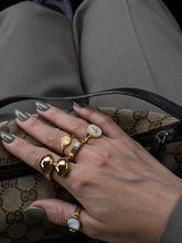 Neva Langais gold ring displayed among other stylish gold rings on a hand with green nails in a handbag.