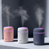 Three portable aroma essential oil diffusers in pink, white, and gray emitting mist with colorful lights.