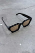 Color Shades - Teddy stylish sunglasses with sleek black frames and brown lenses on a textured surface.